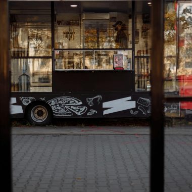 A vibrant food truck parked on a city street, featuring artistic designs and reflections.