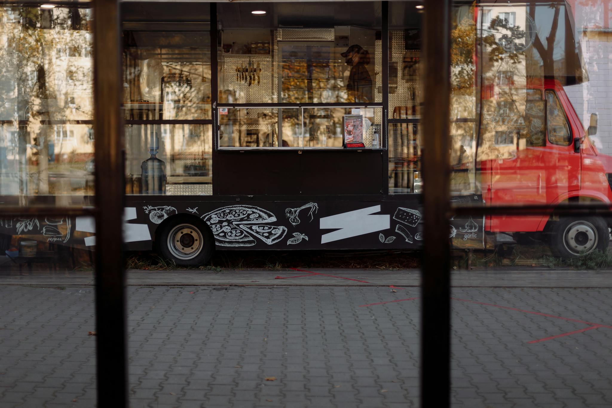 A vibrant food truck parked on a city street, featuring artistic designs and reflections.
